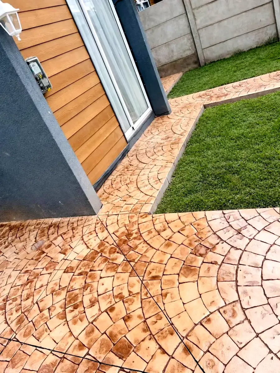 Patio con hormigón estampado en abanico europeo, color beige oscuro, junto al pasto